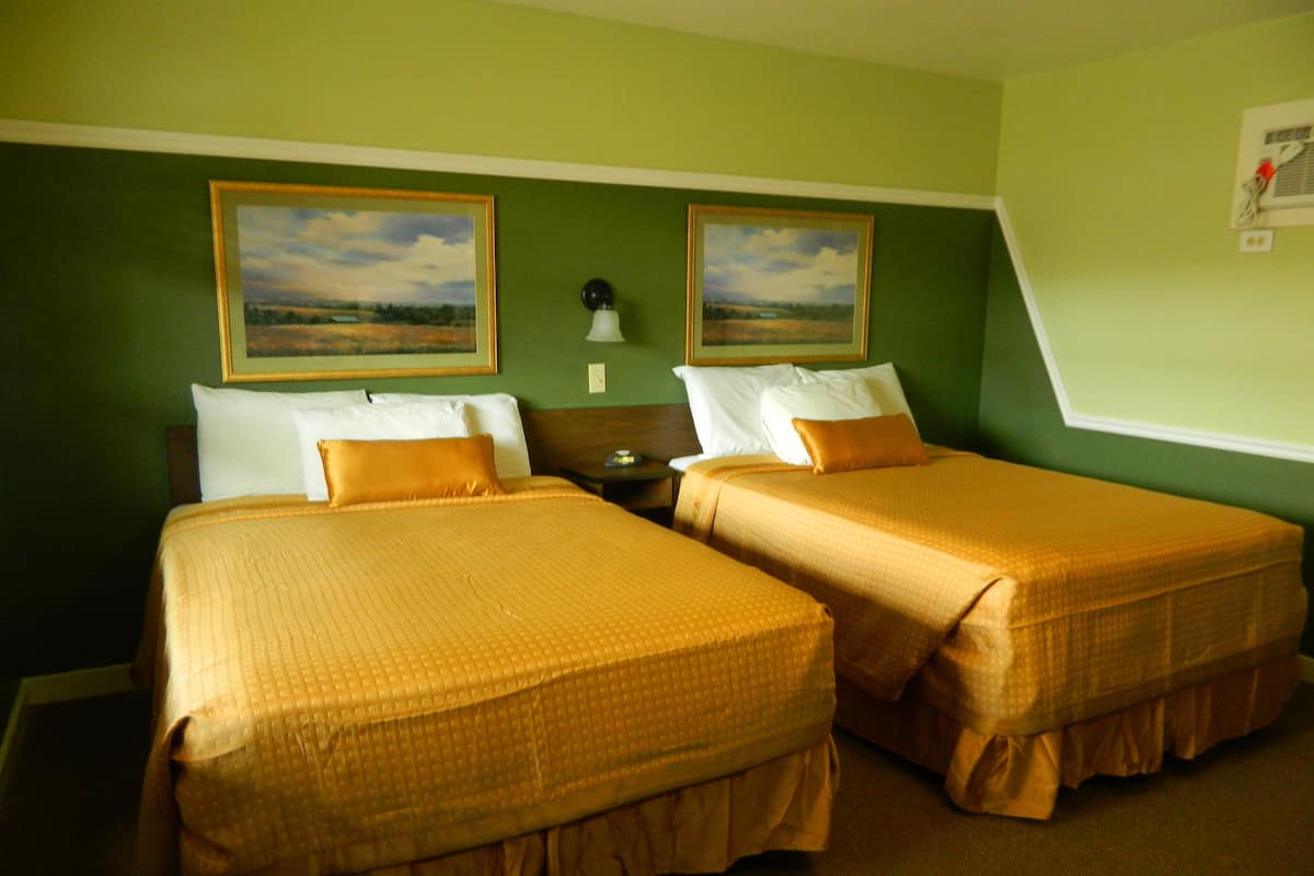 A hotel room with two beds, green walls, and two landscape paintings.