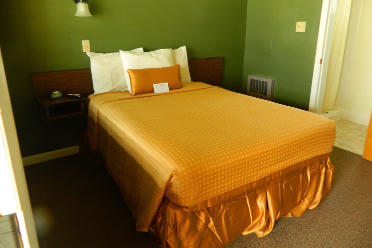 A neatly made bed with a brown bedspread, white pillows, and a wooden headboard.