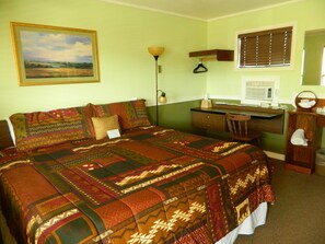 A room with a bed, a desk, a chair, a lamp, a window with blinds, and a painting on the wall.