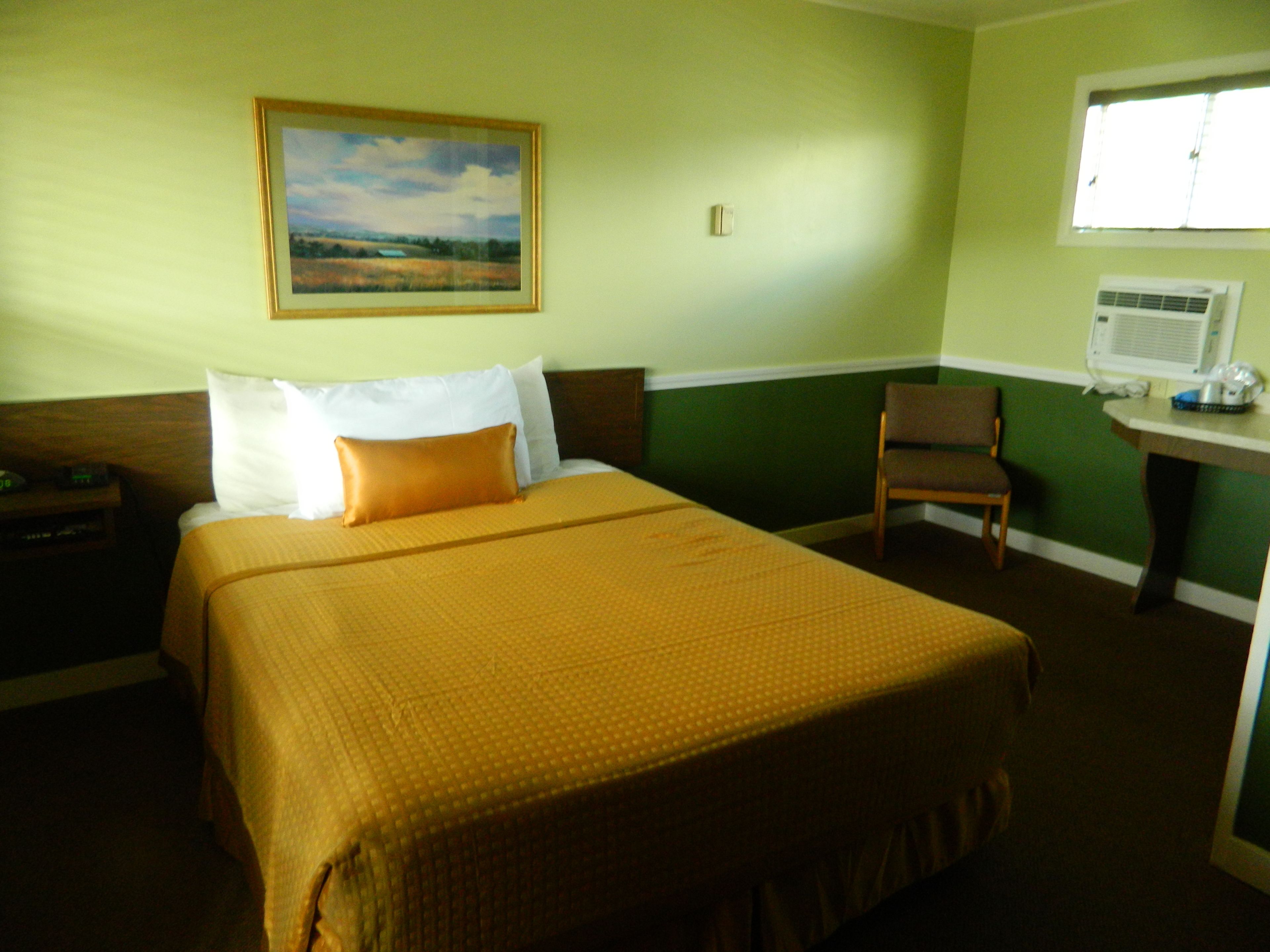 Una habitación de hotel con una cama grande, una silla, un escritorio y un aire acondicionado, además de un cuadro en la pared.