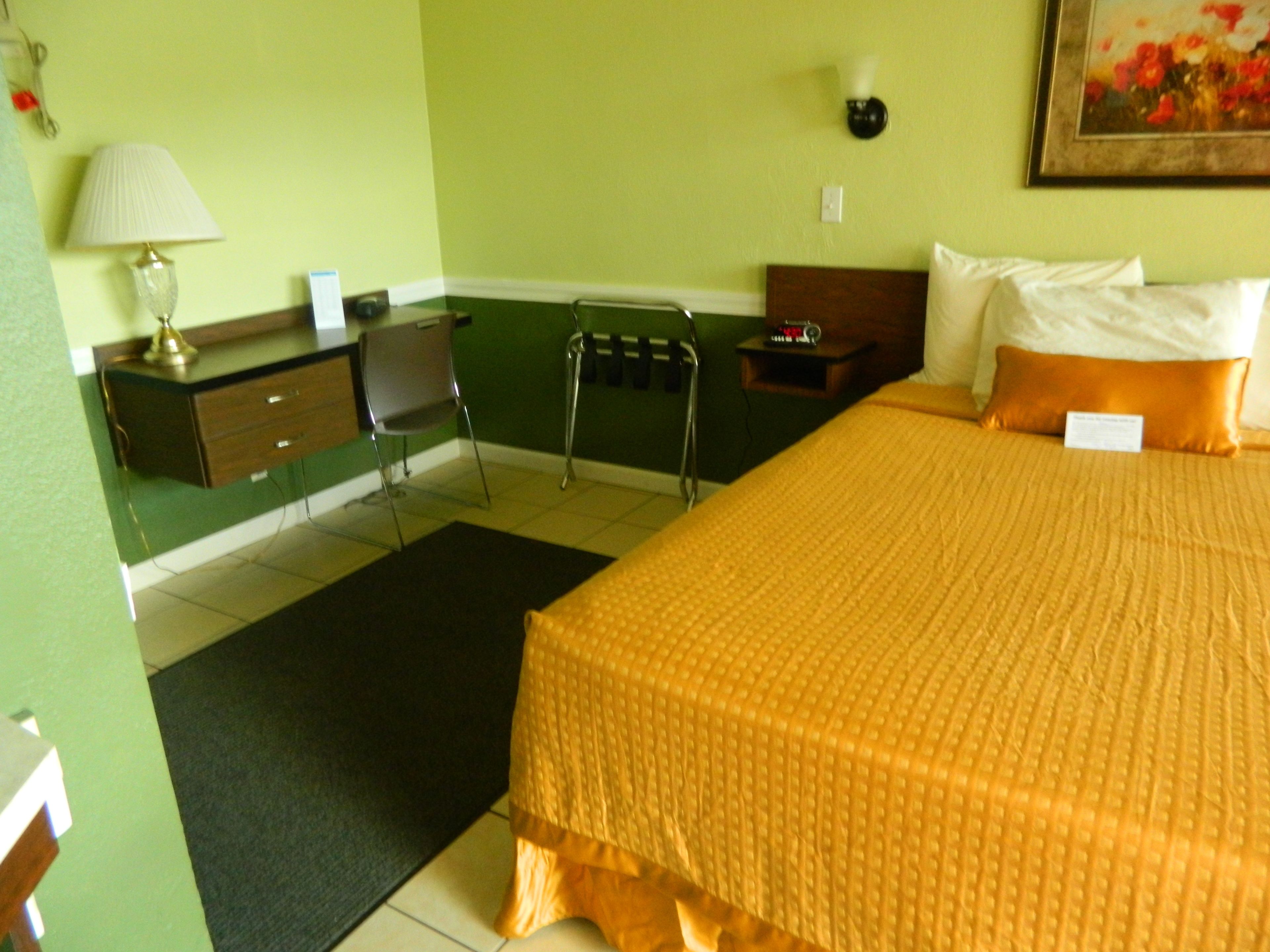 Ein Hotelzimmer mit Bett, Schreibtisch, Stuhl, Lampe und einem Bild an der Wand.