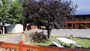 A parking lot with picnic tables, a wooden fence, and a building with a balcony in the background. - Country Motor Inn (Livingston)