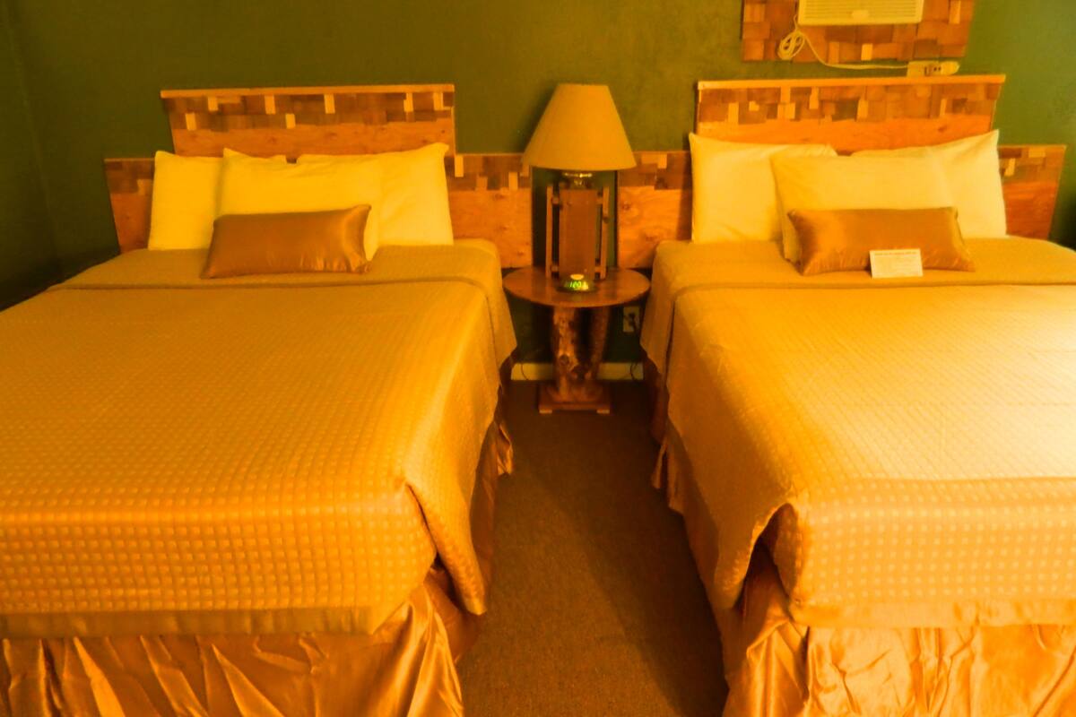 A hotel room with two beds, a nightstand, a lamp, and a wall-mounted TV.