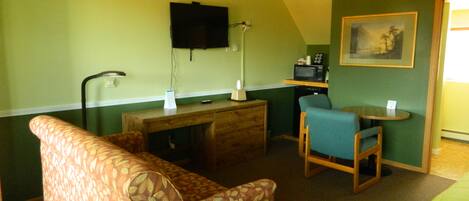 Ein kleines Zimmer mit Schreibtisch, Fernseher, Mikrowelle und Essecke mit Stuhl und Tisch.