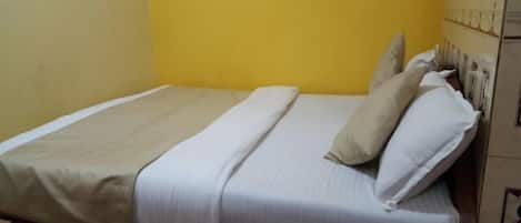 A single-bed room with a beige bedspread, two pillows, and a wooden headboard.