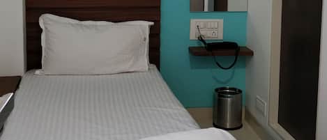 A hotel room with a bed, two remote controls, a framed picture, a mirror, and a door.