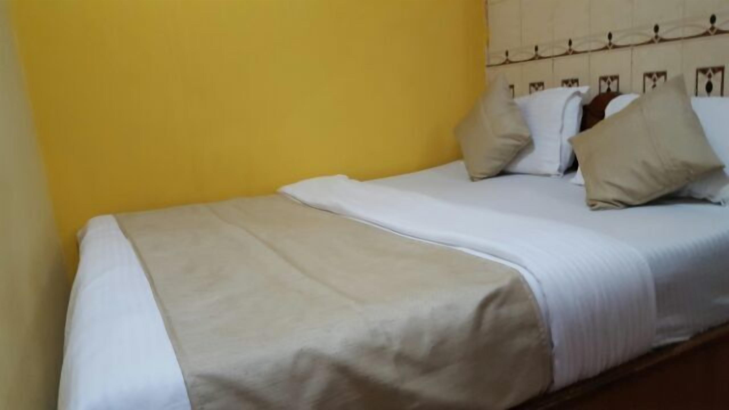 Een eenpersoonsbed met een wit-beige sprei, twee kussens en een hoofdbord met een decoratief patroon.