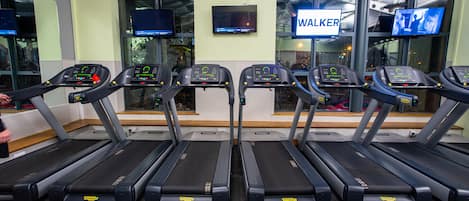 Cuatro cintas de correr en un gimnasio con un letrero que dice 'WALKER' encima y una pantalla de televisión en la pared.