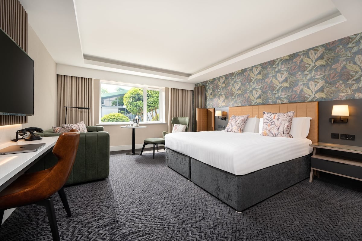 A hotel room with a large bed, a desk with a chair, a TV, and a window with curtains.