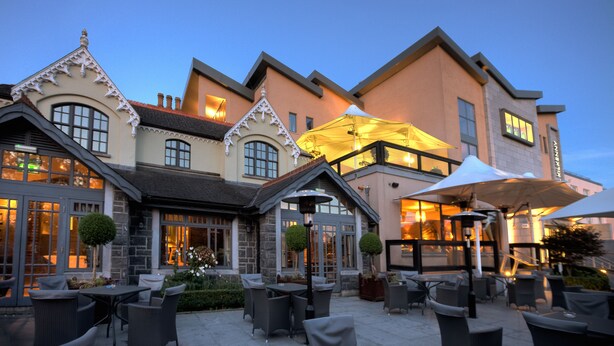 An outdoor patio with wicker furniture and umbrellas, a stone building with a traditional architectural style, and a clear evening sky. - Hotel Kilkenny (Kilkenny)