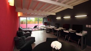 A modern office space with a red accent wall, a black sofa, a round table with a vase, and multiple computer workstations. - Hostal La Buena Vida (Mexico City)