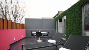 A rooftop lounge area with a black lounge chair, a white table with two chairs, and a red wall. - Hostal La Buena Vida (Mexico City)