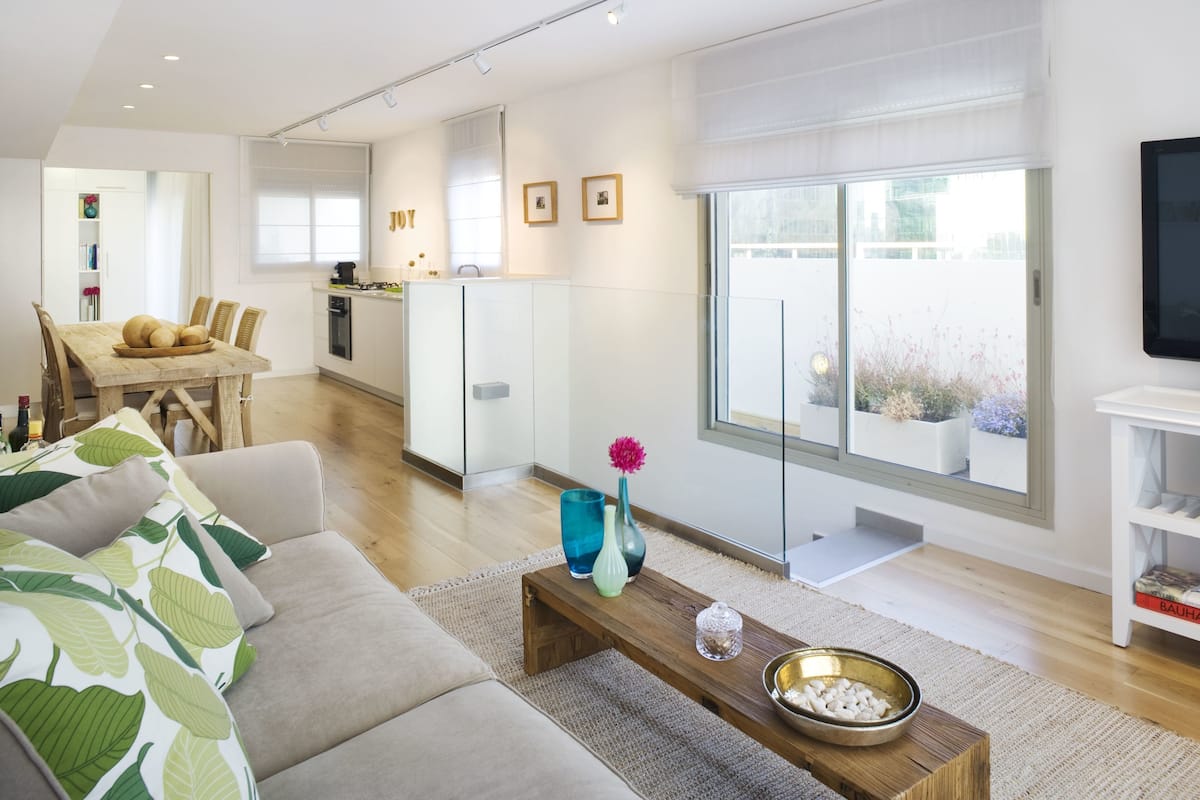 A modern living room with a sofa, coffee table, and a view of the kitchen and dining area.