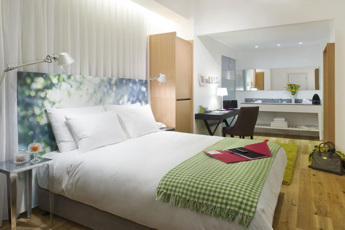 A hotel room with a bed, bedside table, lamp, and a desk with a chair.