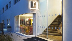 Entrada de hotel con puerta de cristal, una escalera y felpudo con el nombre del hotel.