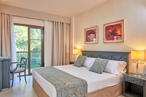 Habitación de hotel con cama, dos lámparas de noche, escritorio, silla y balcón con cortinas.