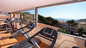 Un gimnàs amb cintes de córrer i equip d'exercici, amb vista a una zona costanera amb edificis i arbres.
