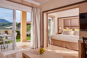 A hotel room with a bed, a TV, a desk with a bowl of fruit, and a balcony with a table and chairs. - Zafiro Cala Mesquida (Capdepera)