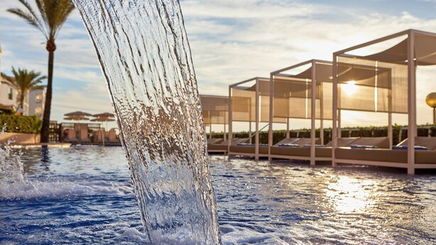 Una piscina amb una font, gandules i un edifici modern al fons.