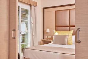 Habitación de hotel con cama, mesita de noche, lámpara y vistas a palmeras a través del ventanal.