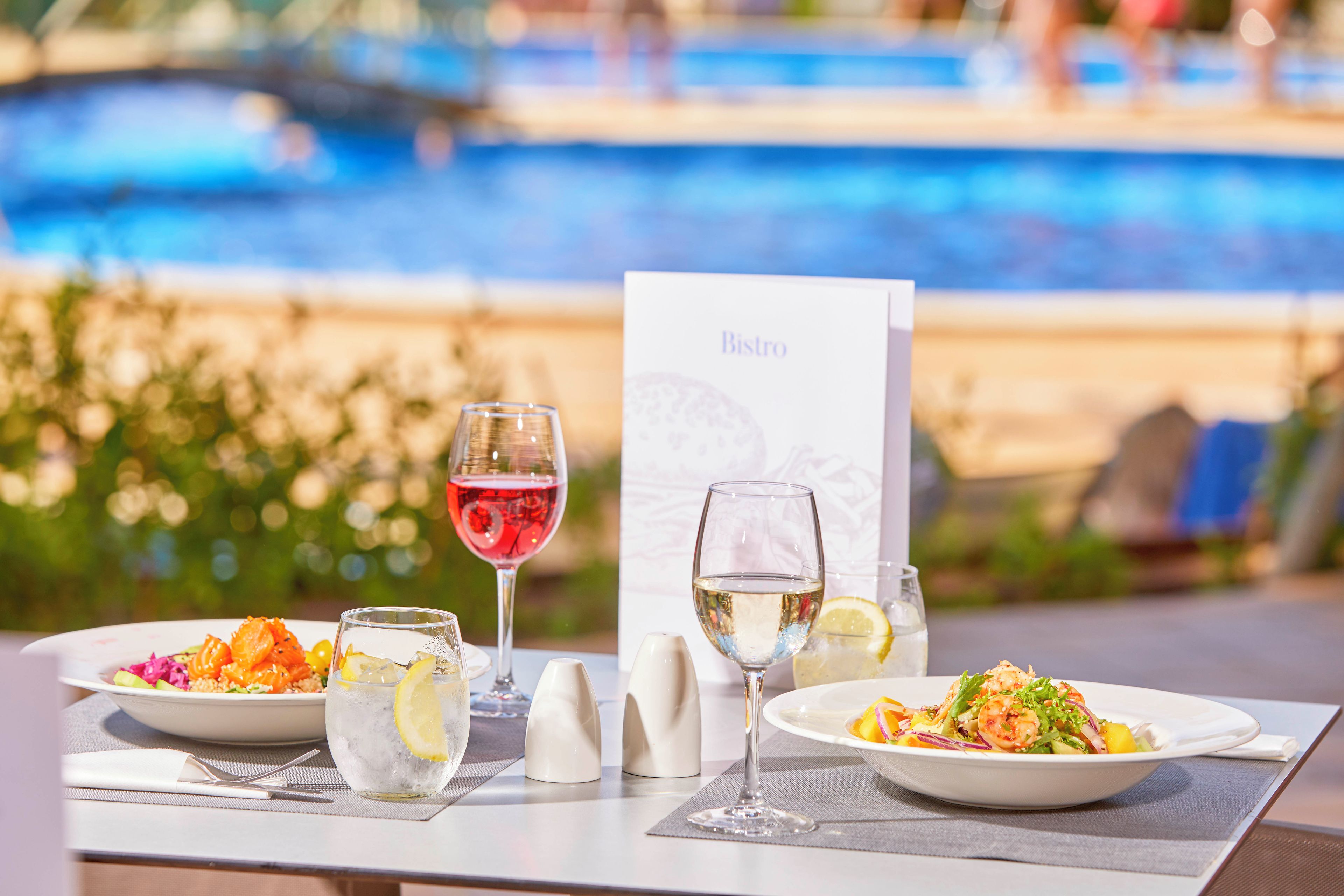 A dining table with two plates of food, two glasses of water, and a menu card.