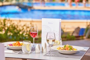 A dining table with two plates of food, two glasses of water, and a menu card. - Zafiro Cala Mesquida (Capdepera)