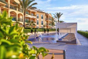 A swimming pool with a water feature, surrounded by a wooden deck and palm trees. - Zafiro Cala Mesquida (Capdepera)