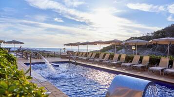 A pool area with lounge chairs and umbrellas, overlooking a body of water.