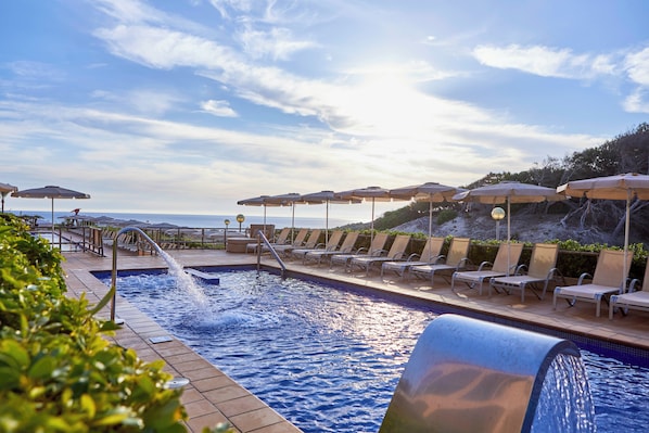 A pool area with lounge chairs and umbrellas, overlooking a body of water.