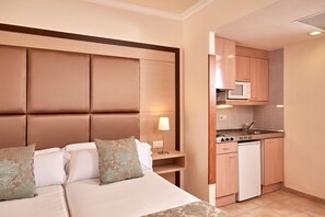 Una habitación de hotel con cama, mesita de noche, lámpara y una kitchenette con microondas y lavavajillas.