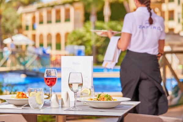 A dining table with two plates of food, two glasses of wine, and a menu card.