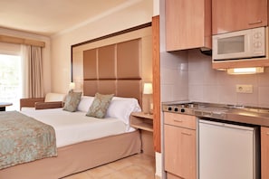 Una camera d'albergo con un letto grande, un comodino, un forno a microonde, un piano cottura e un piccolo frigorifero.