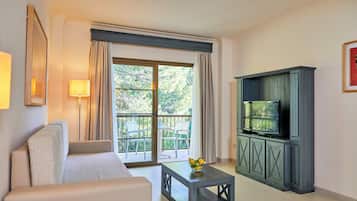 A modern living room with a sofa, a coffee table with fruit, a TV on a cabinet, and a balcony with chairs and curtains.