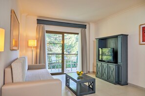 Una sala de estar moderna con un sofá, una mesa de centro con fruta, un televisor sobre un mueble bajo y un balcón con sillas y cortinas.