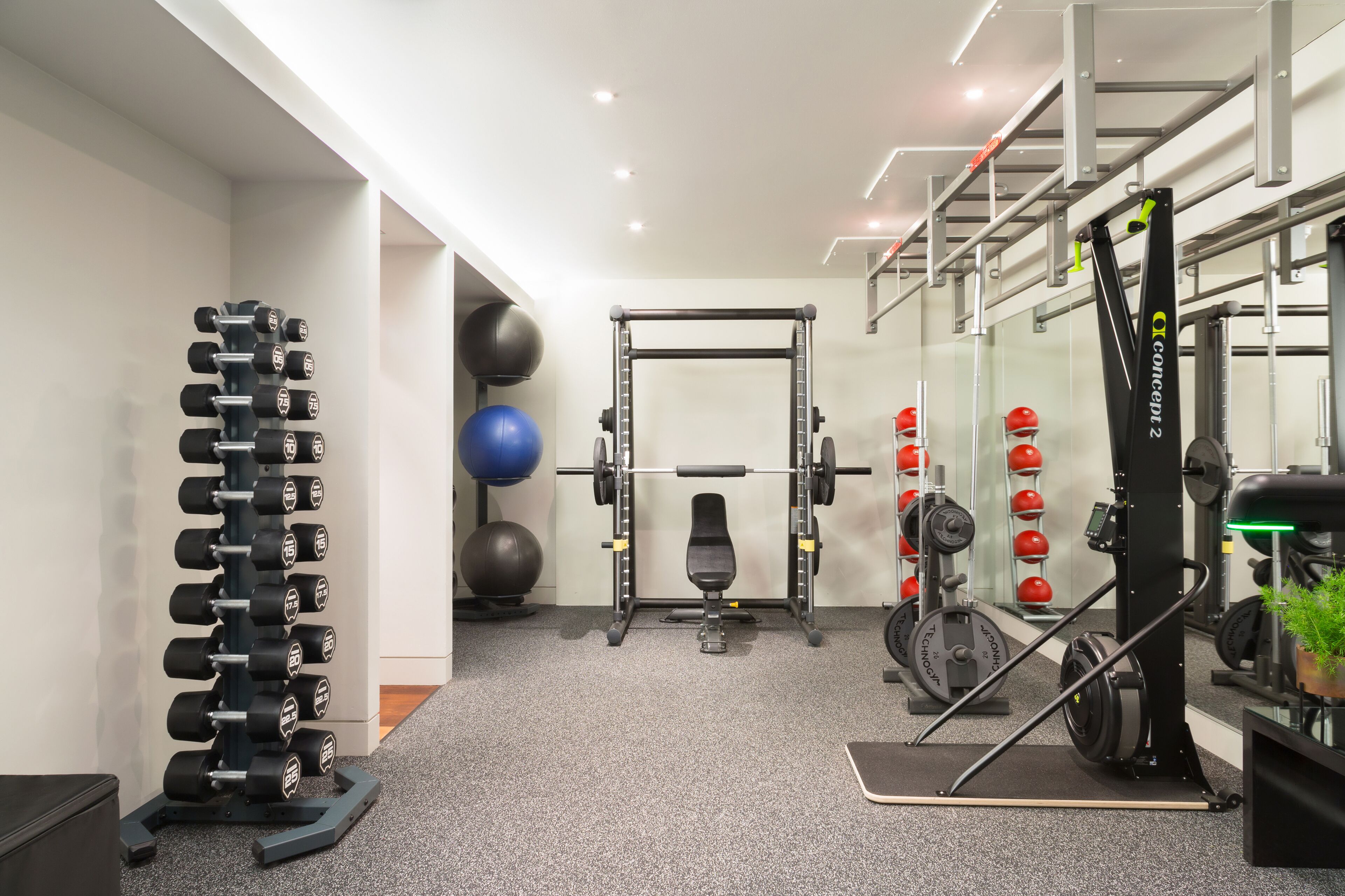 Ett gym med en bänkpress, hantlar, ett knäböjsställ och träningsbollar.