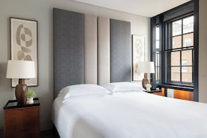 Ein Hotelzimmer mit einem großen Bett, zwei Nachttischen mit Lampen und einem Fenster mit Blick auf Gebäude.