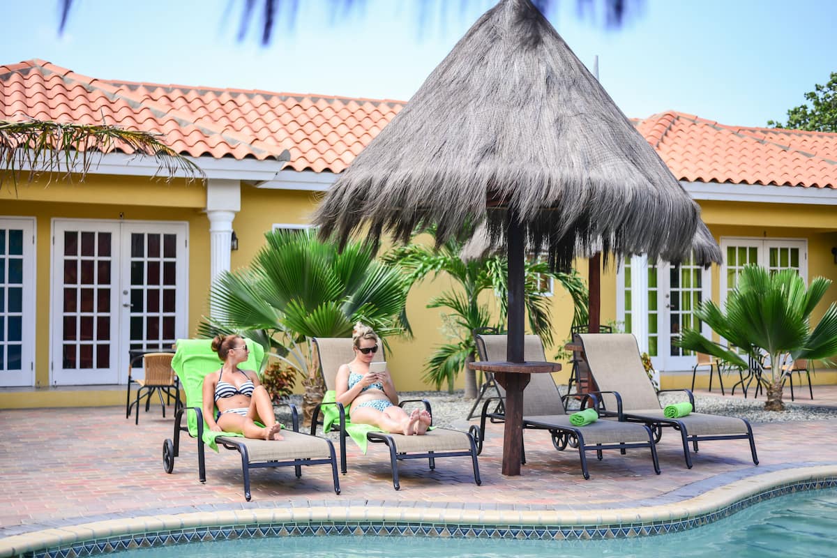 A poolside area with lounge chairs, a thatched umbrella, and a pool.