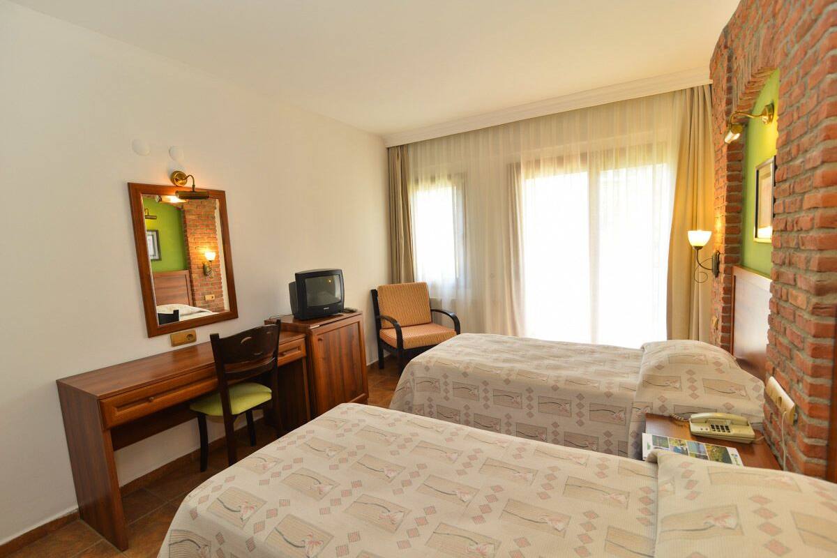 Ett hotellrum med två sängar, ett skrivbord med en stol, en tv och en spegel.