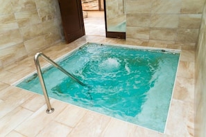 Une piscine intérieure rectangulaire à l’eau claire, entourée de murs et d’un sol recouverts de carreaux de couleur beige.