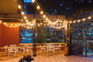 Un espace extérieur aménagé en patio, avec des tables et des chaises, des guirlandes lumineuses et une clôture décorative.