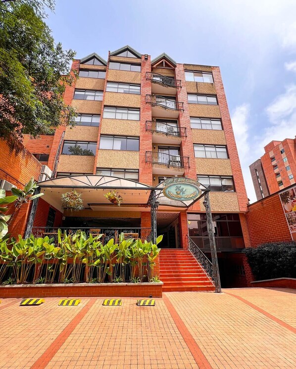 Un hôtel à plusieurs étages, doté d’une façade en briques, de balcons et d’un espace d’entrée abrité agrémenté de plantes.