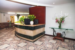 A reception area with a curved reception desk, a glass-top console table, and a wall-mounted sign that reads "Solar Hotel Centro Empresales."