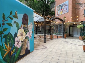 A courtyard with a mural of flowers and a bird, outdoor seating, and string lights.