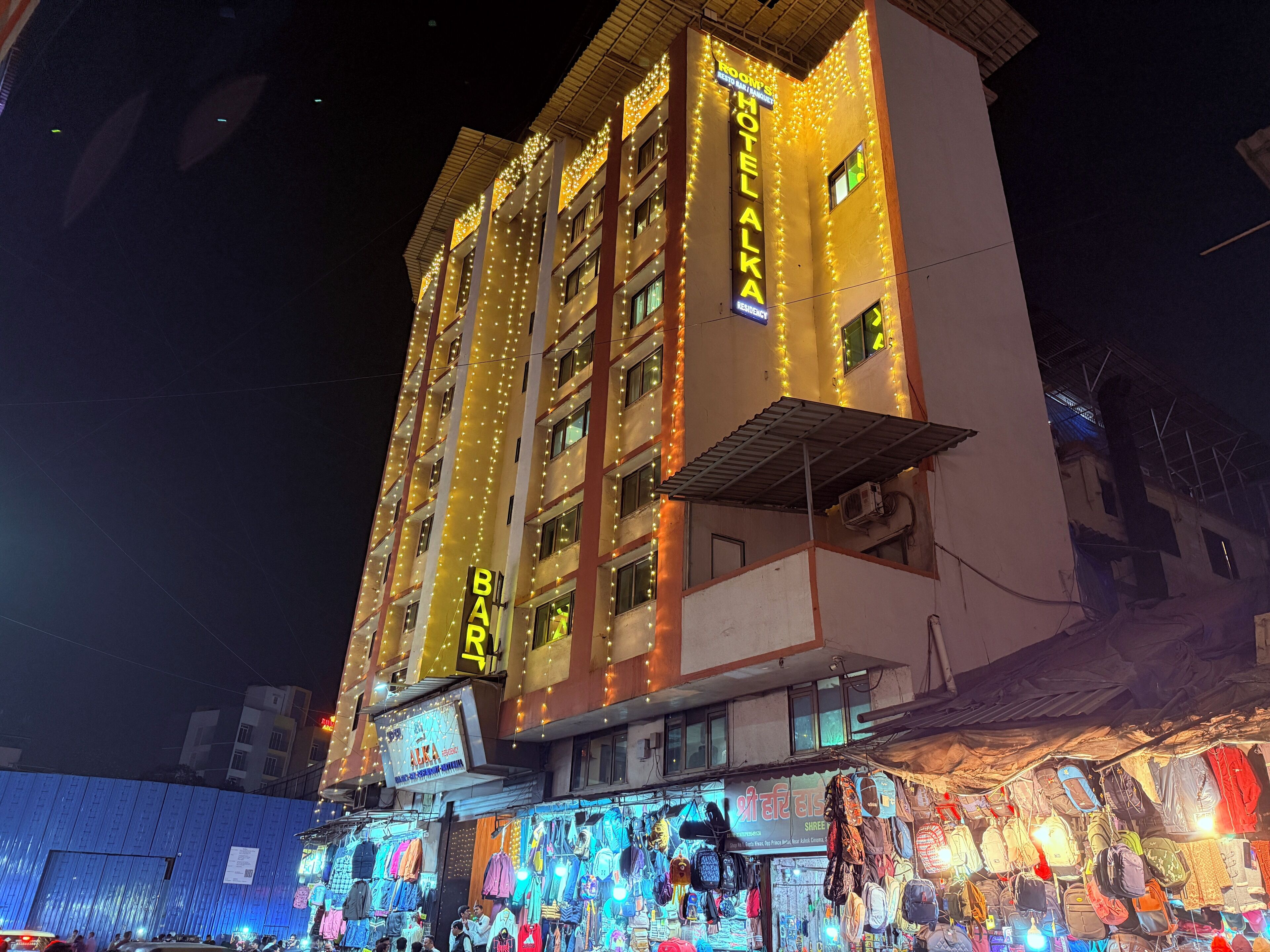 A hotel with multiple floors, balconies, and a ground-level market selling various items.