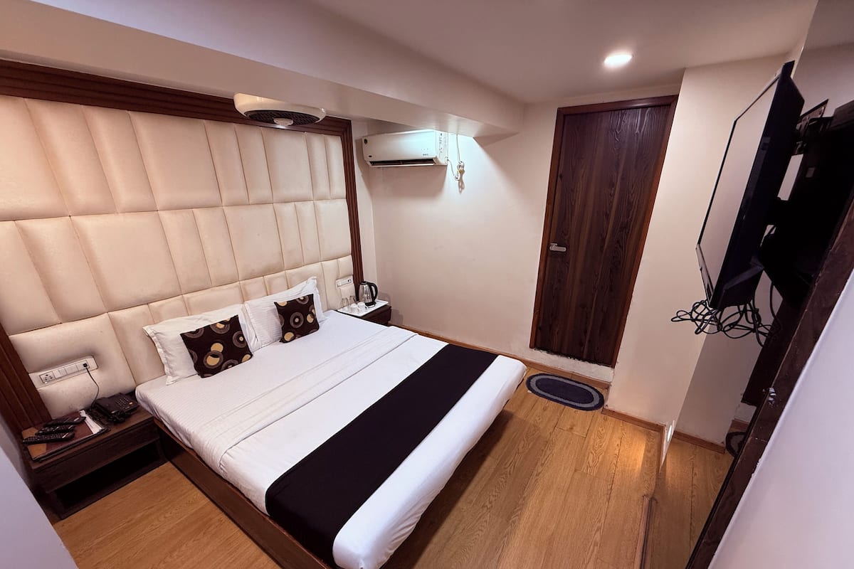 A hotel room with a large bed, a bedside table with a lamp, a wardrobe, and a television mounted on the wall.