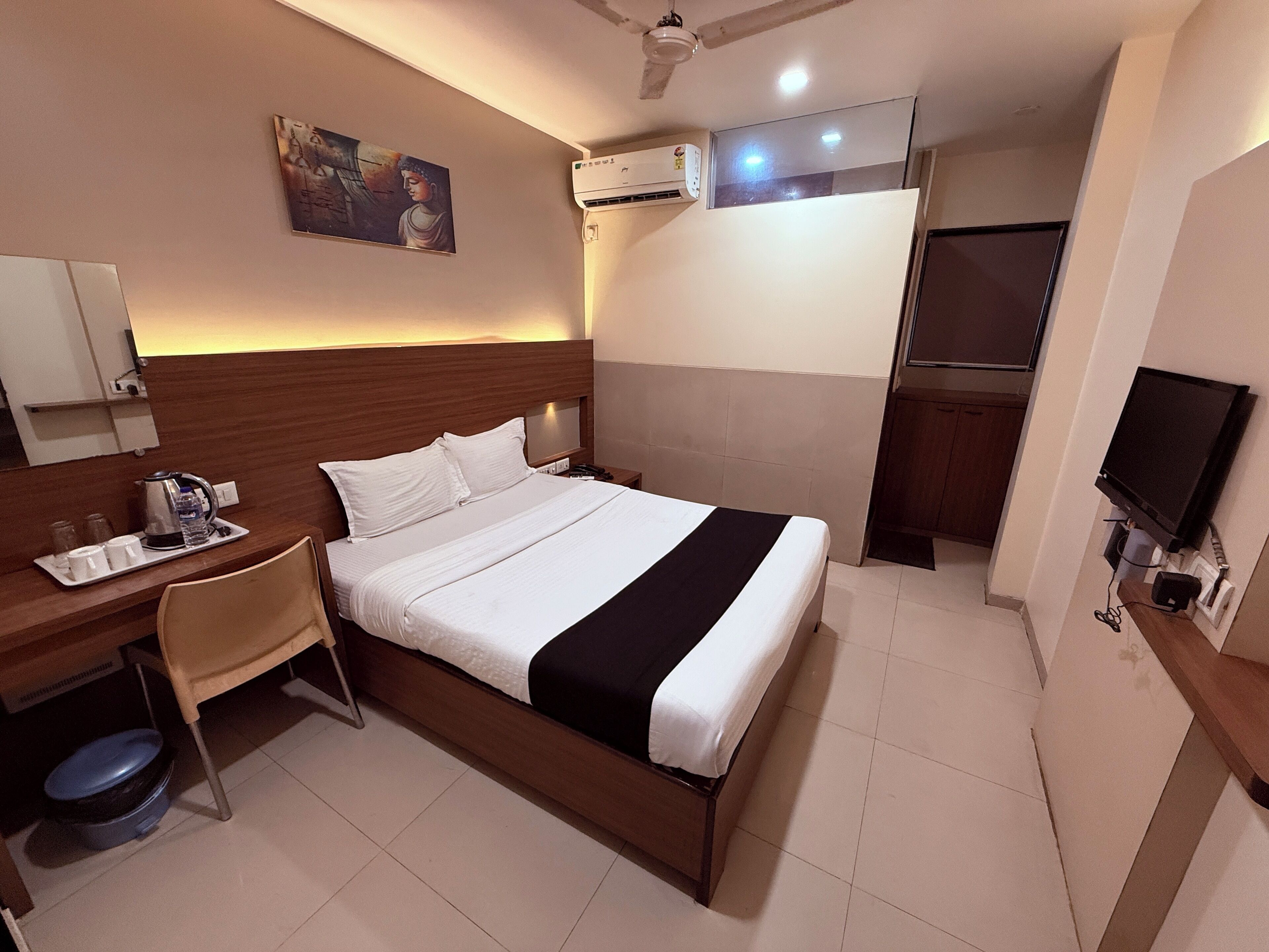 A hotel room with a bed, a desk with a chair, a television, and an air conditioning unit.