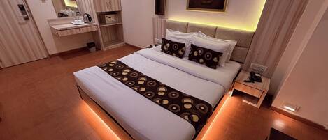 Quarto de hotel moderno com cama grande, mesas de cabeceira, penteadeira com espelho e uma obra de arte pendurada na parede.