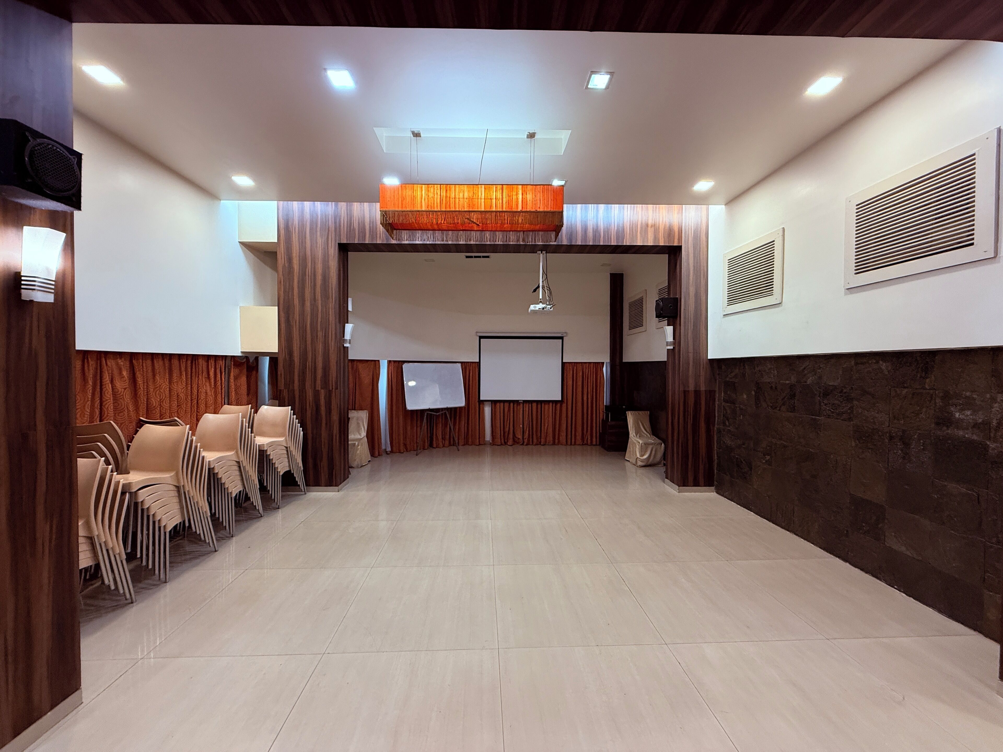 Un salón de conferencias con escenario, sillas, proyector y una pizarra.