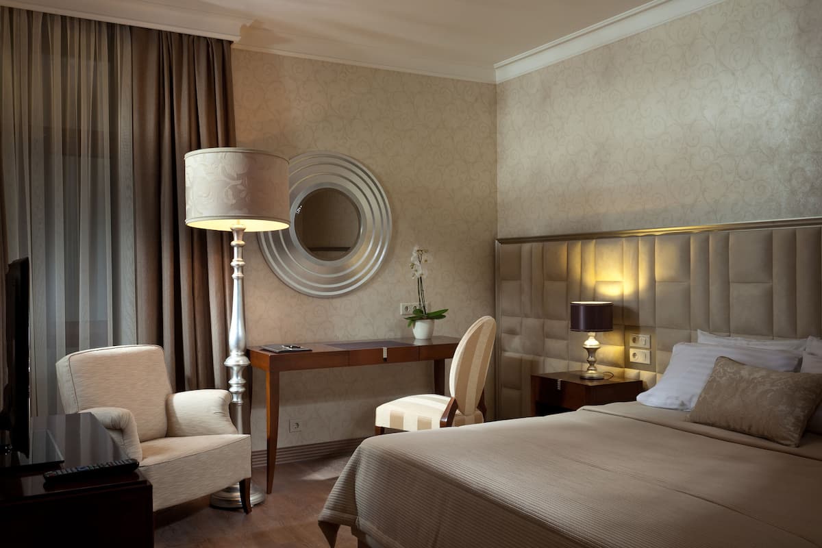 A hotel room with a bed, a desk, a chair, a lamp, and a TV.
