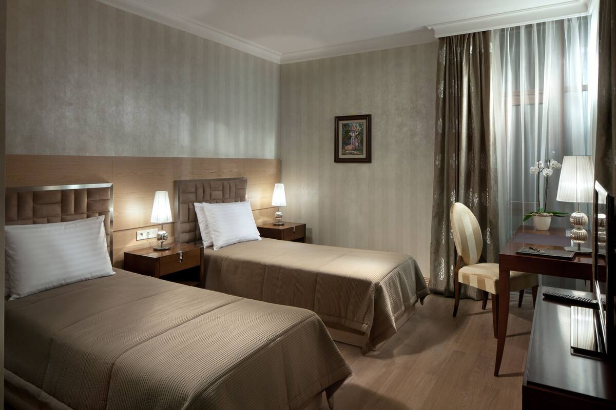 A hotel room with two beds, a desk, a chair, and a nightstand with lamps.